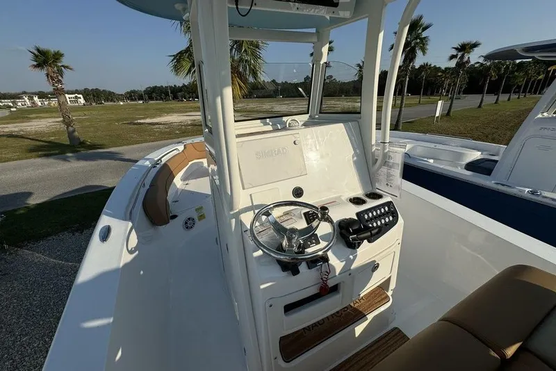 Slide: The Image of 2024 NauticStar 252 Legacy boat interior with steering console and seating, set outdoors. - 21