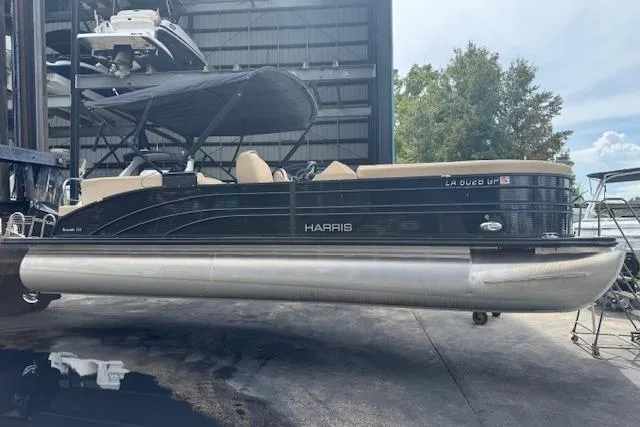 The Image of 2023 Harris Sunliner 250 pontoon boat in storage, featuring sleek black design and spacious seating. - 1