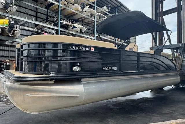 Slide: The Image of 2023 Harris Sunliner 250 pontoon boat in storage, featuring sleek black design and canopy. - 4