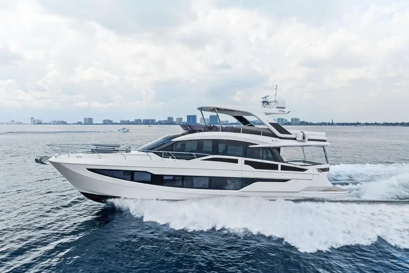 Slide: The Image of 2022 Galeon 640 Fly yacht cruising on open water with city skyline backdrop. - 15