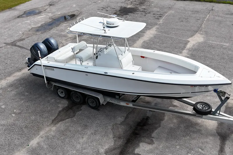 Slide: The Image of White 2003 Jupiter 27 boat on trailer with dual engines, parked on concrete surface. - 11