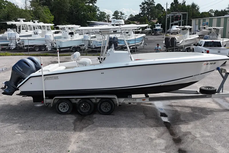 Slide: The Image of 2003 Jupiter 27 boat on trailer, parked in marina with other boats in background. - 9