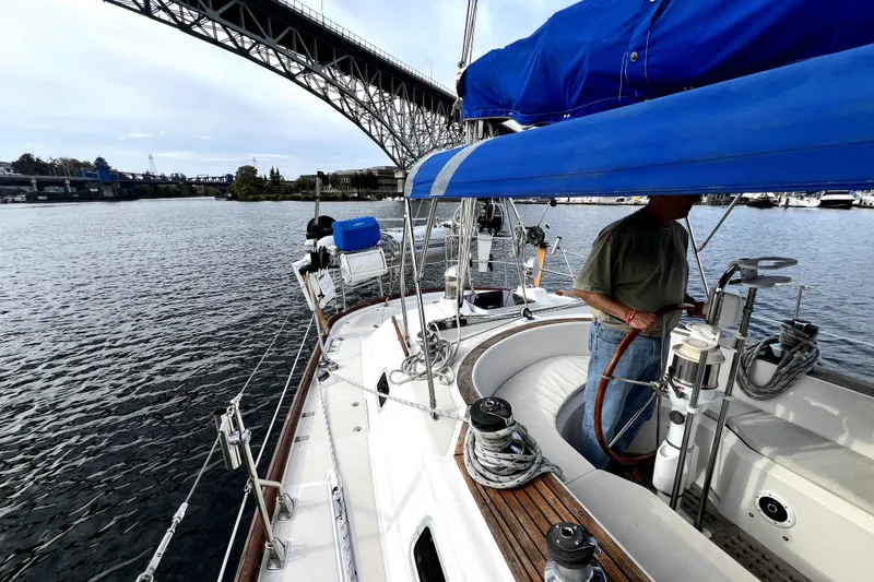 Slide: The Image of 1989 Taswell 43 sailboat under bridge, featuring blue canopy and scenic waterfront view. - 17