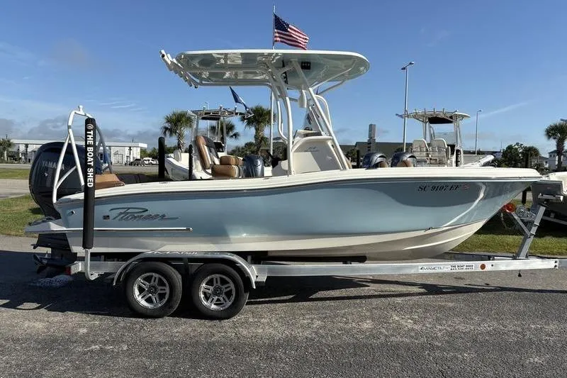 Slide: The Image of 2025 Pioneer 202 Islander boat on trailer, parked outdoors with American flag. - 4