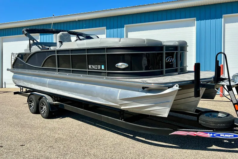 The Image of 2018 Manitou MD 25 TriToon pontoon boat on trailer, parked outside blue building. - 1
