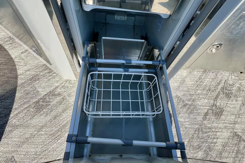 Slide: The Image of Open storage compartment on 2018 Manitou MD 25 TriToon boat, featuring a wire basket. - 3