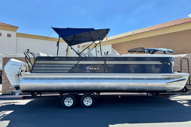 The Image of 2022 Crest Classic DLX 240 SLRC pontoon boat on trailer, blue canopy, parked outdoors. - 0