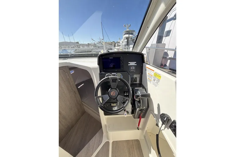 Slide: The Image of 2023 Bayliner Trophy T25 Explorer interior with seating and table, docked at marina. - 11