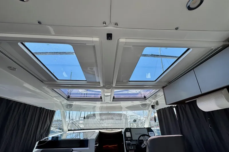 Slide: The Image of 2024 Beneteau Antares 11 interior with gray seating, wooden table, and striped cushions. - 10
