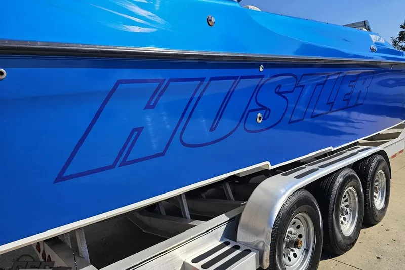 Slide: The Image of Blue 2002 Hustler 388 SLINGSHOT boat on trailer, showcasing bold branding. - 10