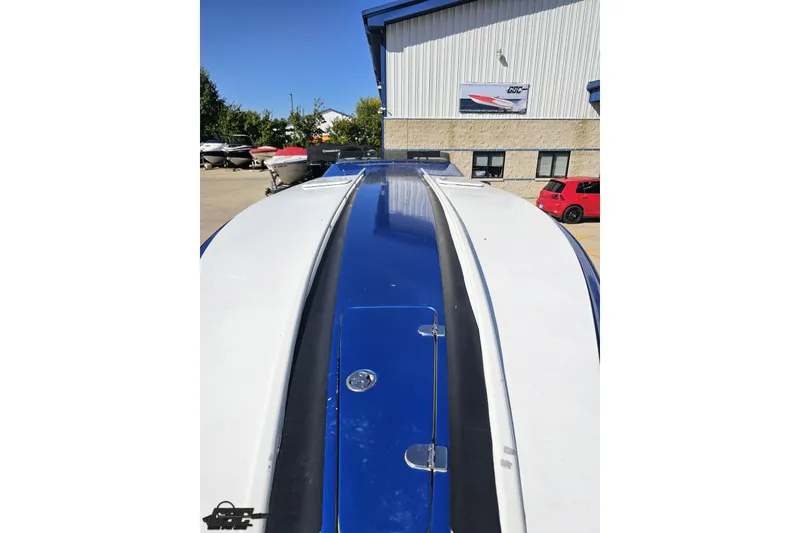 Slide: The Image of 2002 Hustler 388 SLINGSHOT boat, blue and white, parked outdoors near a building. - 18