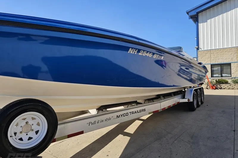 Slide: The Image of 2002 Hustler 388 SLINGSHOT boat on trailer, blue and white, parked outside a building. - 21
