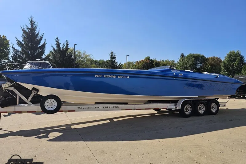 Slide: The Image of 2002 Hustler 388 SLINGSHOT speedboat on trailer, vibrant blue, parked outdoors. - 22