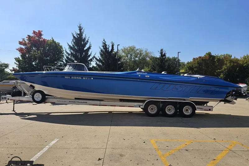 Slide: The Image of 2002 Hustler 388 SLINGSHOT speedboat on trailer, vibrant blue, parked outdoors. - 23