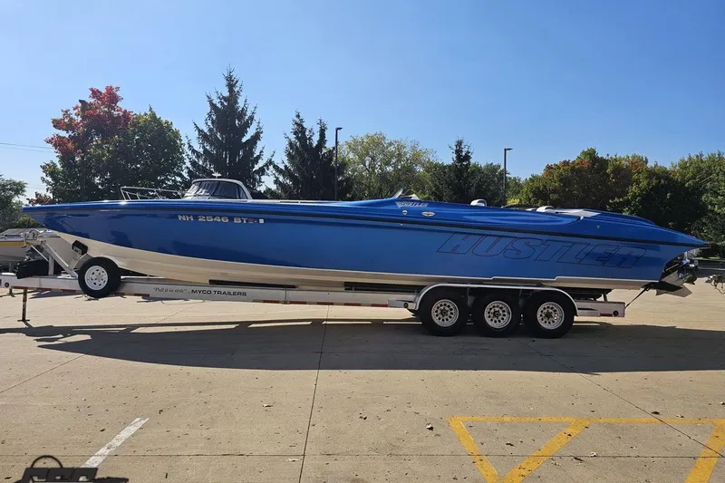 Slide: The Image of 2002 Hustler 388 SLINGSHOT boat on trailer, vibrant blue, parked outdoors. - 24