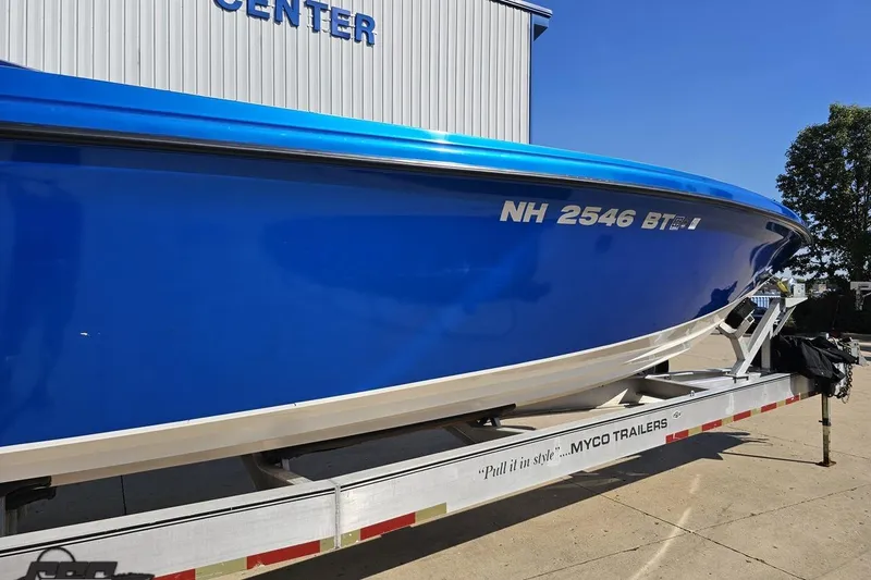 Slide: The Image of 2002 Hustler 388 SLINGSHOT boat on trailer, vibrant blue hull, parked outdoors. - 4