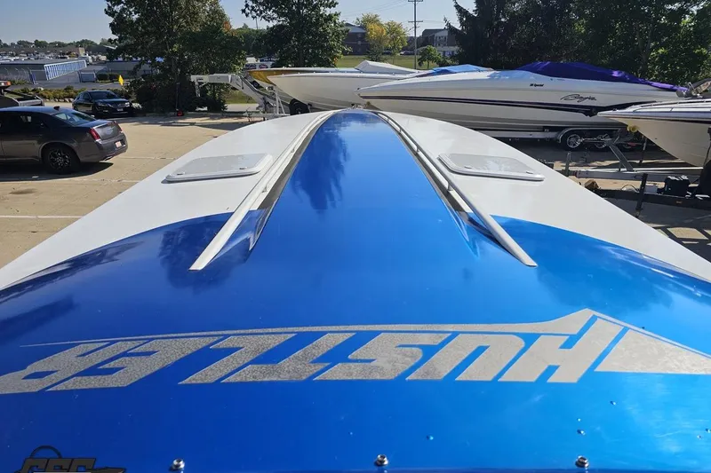 Slide: The Image of 2002 Hustler 388 SLINGSHOT boat with blue and white design in a parking area. - 60