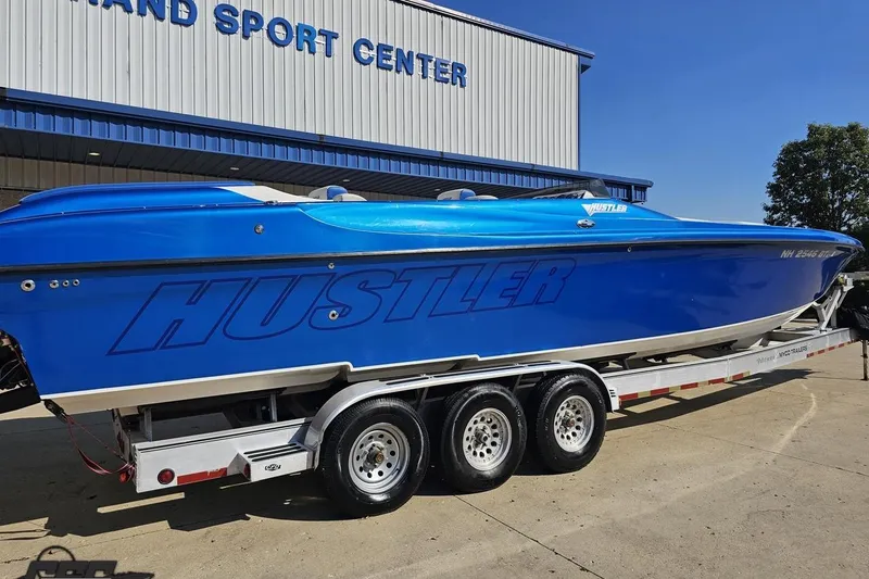 Slide: The Image of 2002 Hustler 388 SLINGSHOT speedboat in vibrant blue on a trailer at a sport center. - 9