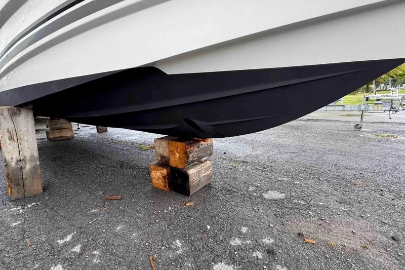 Slide: The Image of 2019 Monterey 295 Sport Yacht on wooden blocks, showing hull and trailer in background. - 14