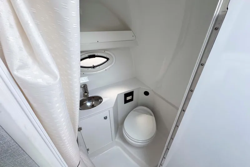 Slide: The Image of 2019 Monterey 295 Sport Yacht bathroom with toilet, sink, and porthole window. - 28