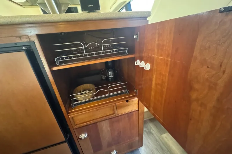 Slide: The Image of 1998 Carver 530 Voyager Pilothouse kitchen cabinet with open wooden door and pull-out shelves. - 60