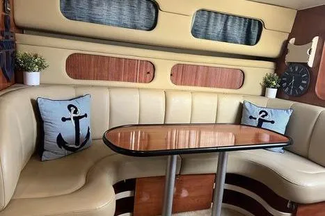 Slide: The Image of 2002 Rinker 342 Fiesta Vee interior with beige seating, anchor-themed pillows, and wooden table. - 9