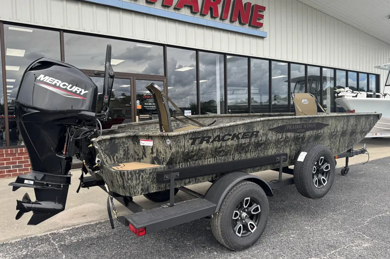 Slide: The Image of 2026 Tracker Grizzly 1650 T Prairie Wings Edition boat with Mercury engine, parked outside a marine store. - 2