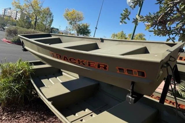 Slide: The Image of 2026 Tracker Grizzly 10 Jon boat, olive green, parked outdoors with trees in the background. - 1