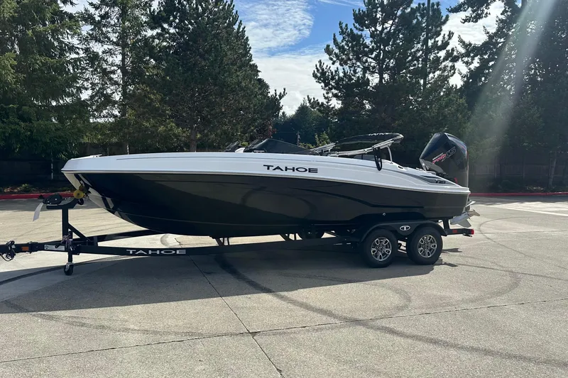 Slide: The Image of 2026 Tahoe T21 boat on trailer, parked outdoors with trees in background. - 2