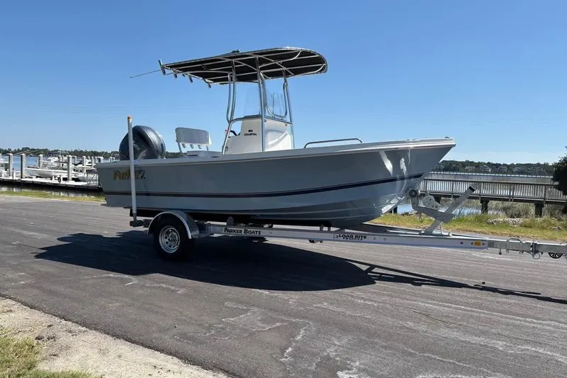 The Image of 2026 Parker 180 Coastal boat on trailer, parked near marina under clear blue sky. - 1