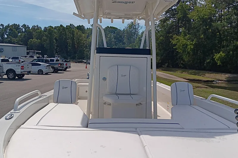 Slide: The Image of 2026 Ranger 2360 Bay boat with white seating, parked near trees and vehicles. - 18