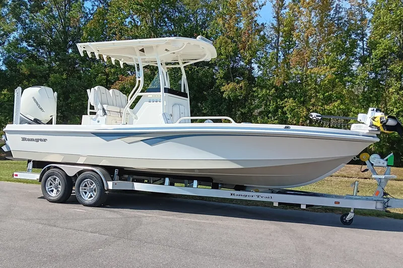 Slide: The Image of 2026 Ranger 2360 Bay boat on trailer, parked outdoors with trees in background. - 2