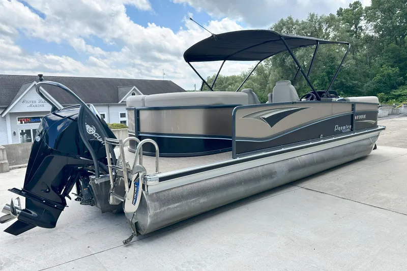 Slide: The Image of 2021 Premier 250 Solaris RE pontoon boat with canopy and outboard motor, parked outdoors. - 2