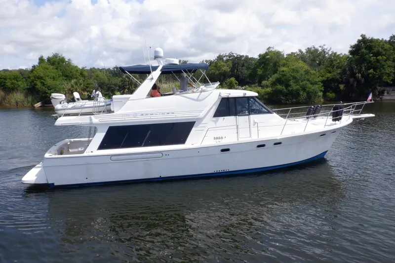 Slide: The Image of 1998 Bayliner 4788 Pilot House Motoryacht cruising on a calm river with lush greenery. - 4