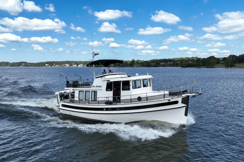 The Image of 2000 Nordic Tug 42 Flybridge cruising on a scenic river with lush green trees. - 0