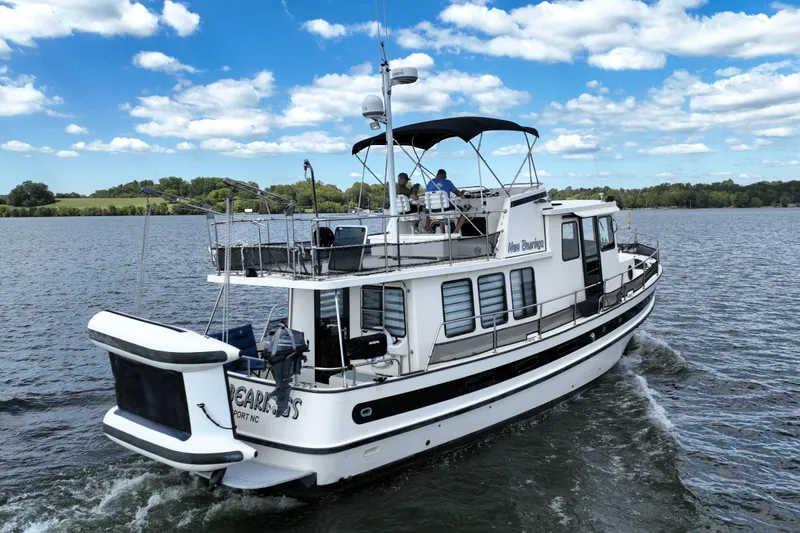 Slide: The Image of 2000 Nordic Tug 42 Flybridge cruising on a scenic lake under a clear blue sky. - 2