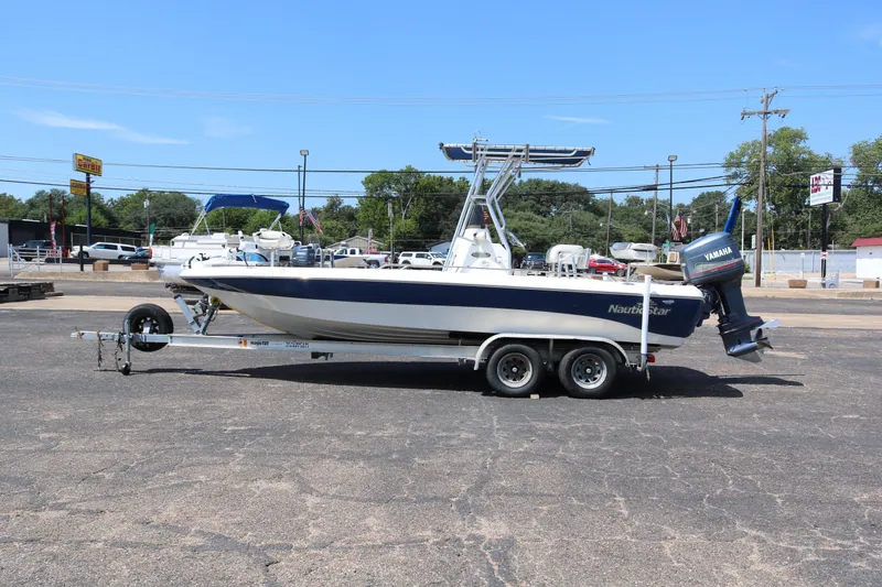 Slide: The Image of 2005 NauticStar 2200 Nautic Bay boat on trailer, parked in a lot under clear blue sky. - 4