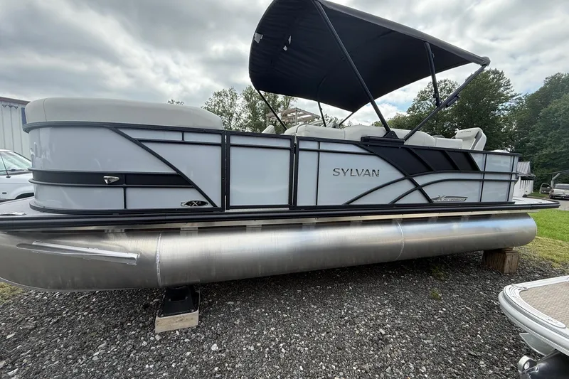 The Image of 2026 SLYVAN X-3 Party Fish pontoon boat with canopy, parked on gravel. - 0