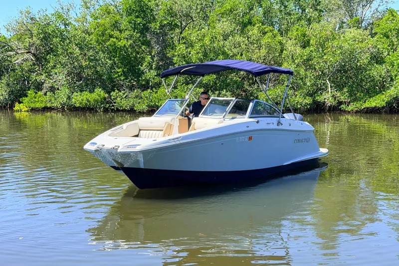 Slide: The Image of 2018 Cobalt 23SC boat cruising on a calm river with lush greenery. - 2