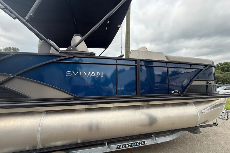 Slide: The Image of 2026 Sylvan L-3 RLZ DH pontoon boat with blue and silver design, parked outdoors. - 5