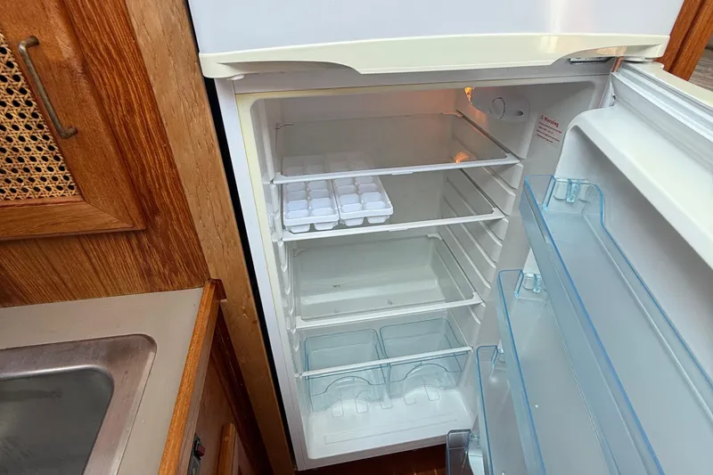 Slide: The Image of Empty refrigerator inside 1983 Bayliner 3870 Motoryacht, featuring wooden cabinetry and ice trays. - 7
