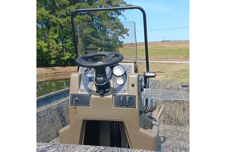 Slide: The Image of 2026 Tracker Grizzly 1860 CC boat console with steering wheel and gauges, near a pond. - 9