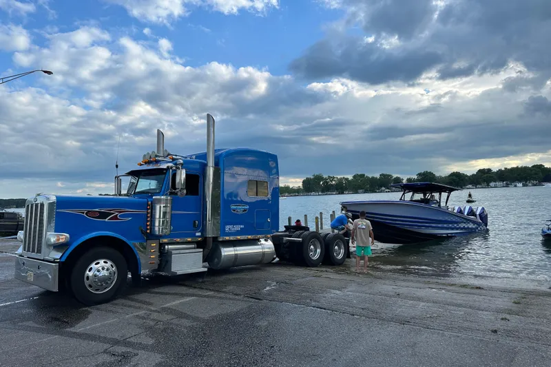 Slide: The Image of Blue truck towing 2025 Nor-Tech 390 Sport boat at lakeside under cloudy sky. - 7