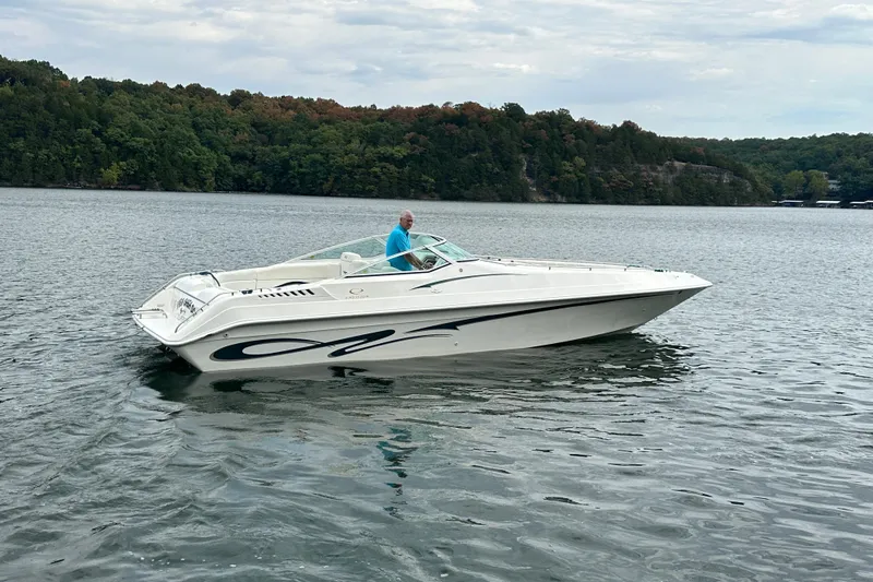 Slide: The Image of 1999 Envision 3200 Intruder boat on a calm lake with forested shoreline. - 10