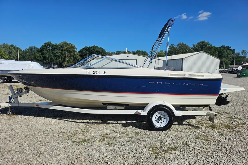 Slide: The Image of 2004 Bayliner 215 Bowrider boat on trailer, parked outdoors under clear blue sky. - 0
