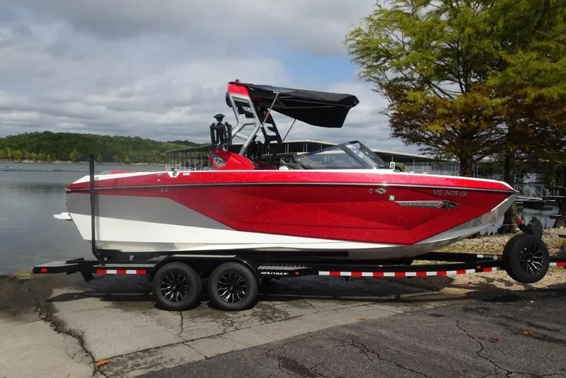Slide: The Image of 2021 Nautique Super Air Nautique G23 boat on trailer by a lake. - 1