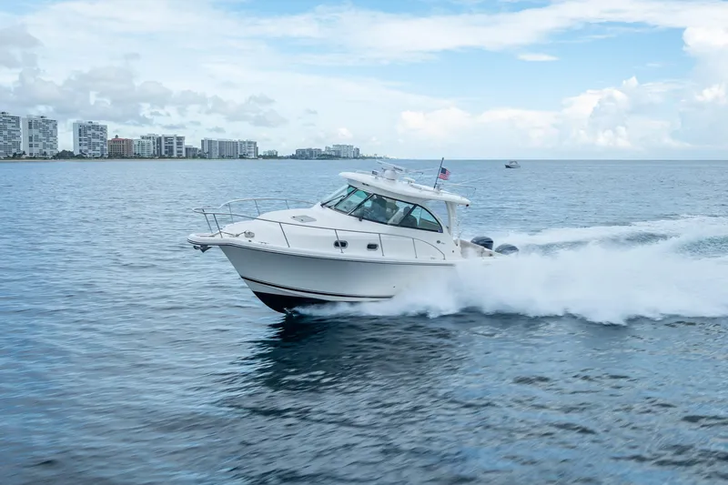 Slide: The Image of 2011 Pursuit OS 345 Offshore boat cruising on open water with city skyline backdrop. - 23