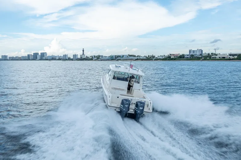 Slide: The Image of 2011 Pursuit OS 345 Offshore boat cruising on open water with city skyline backdrop. - 29