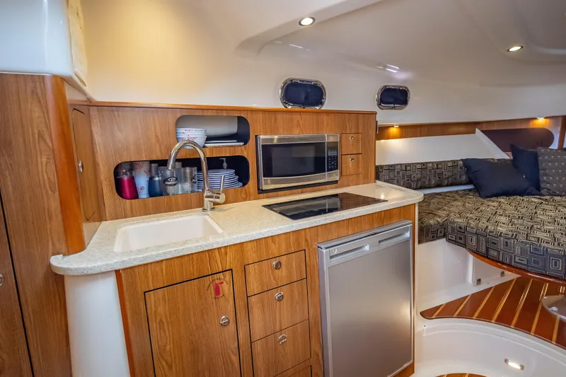 Slide: The Image of 2011 Pursuit OS 345 Offshore boat interior with kitchenette, sink, microwave, and cozy seating area. - 69