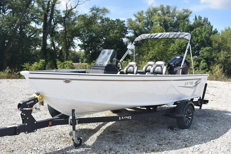 Slide: The Image of 2026 Lund 1800 Explorer SS boat on trailer, parked outdoors, with trees in background. - 2